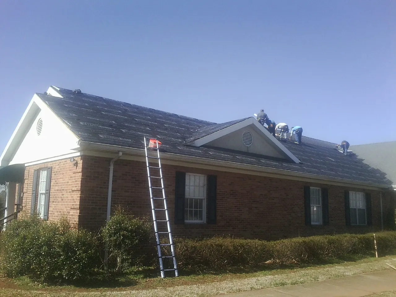 Crew tearing shingles off a brick ranch roof with a ladder set — Metal Roof Repair work by our crew in Bloomfield Hills