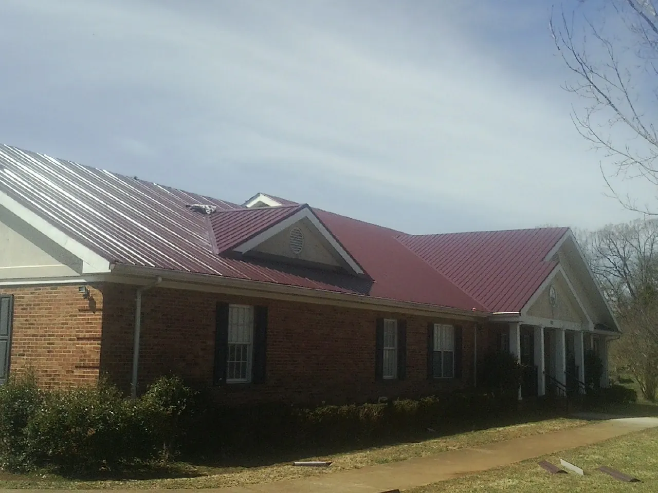 Red metal roof with gabled entries on a long brick building, from a Hail Damage Roof Repair job in Bloomfield Hills