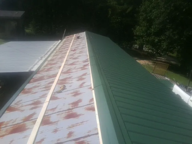 Old rusted panels beside newly installed green metal roofing — Wind Damage Roof Repair by Roofing Brothers in Bloomfield Hills
