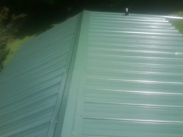 New green metal panels meeting at the ridge of a roof — Flat Roof Repair work by our crew in Bloomfield Hills