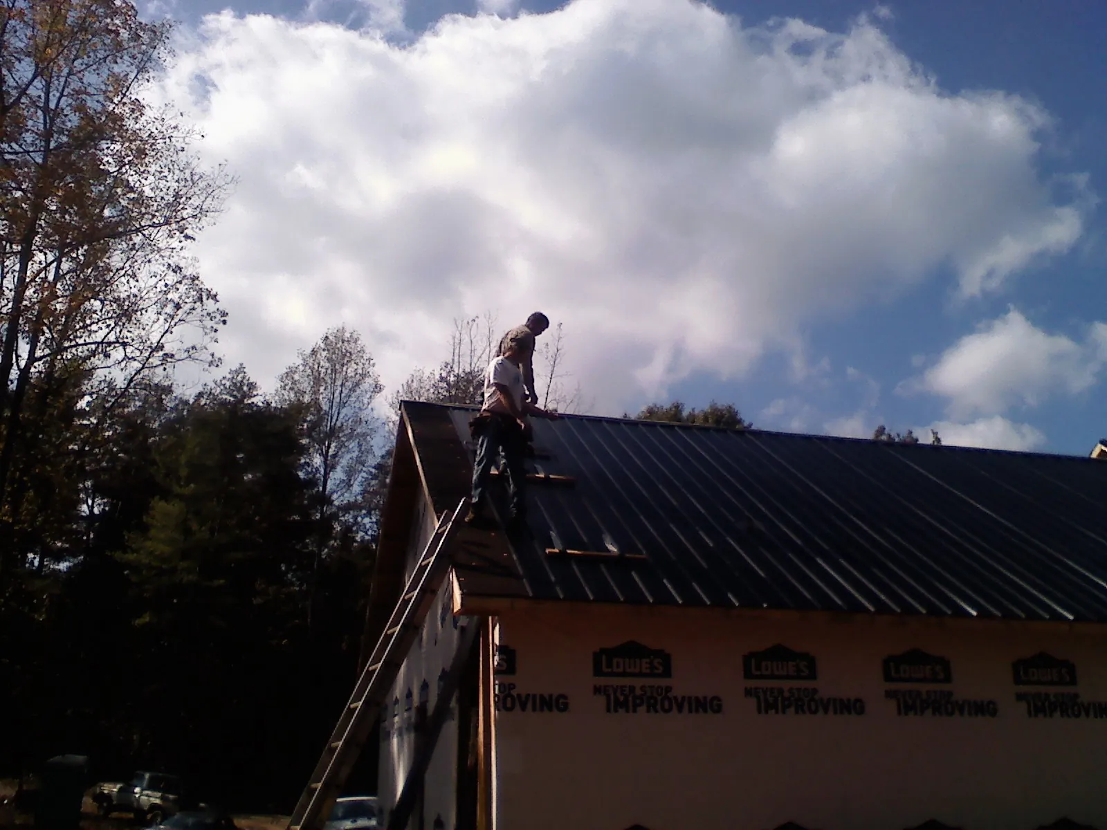 Roofer fastening dark metal panels high against a cloudy sky, from a Roof Inspection job in Bloomfield Hills