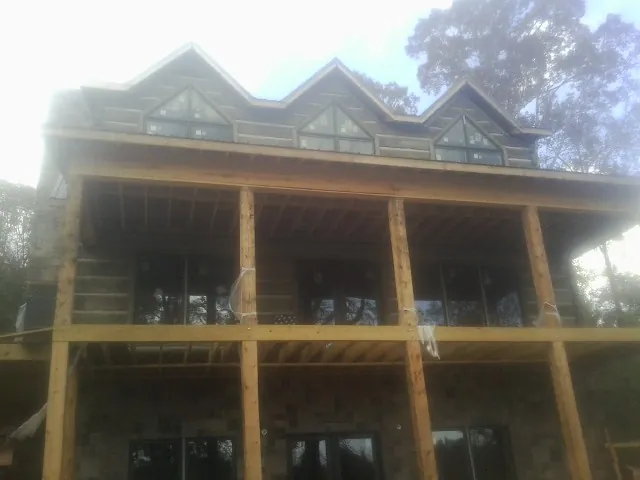Dormers and porch framing on a large log home under construction — Roof Coating work by our crew in Bloomfield Hills