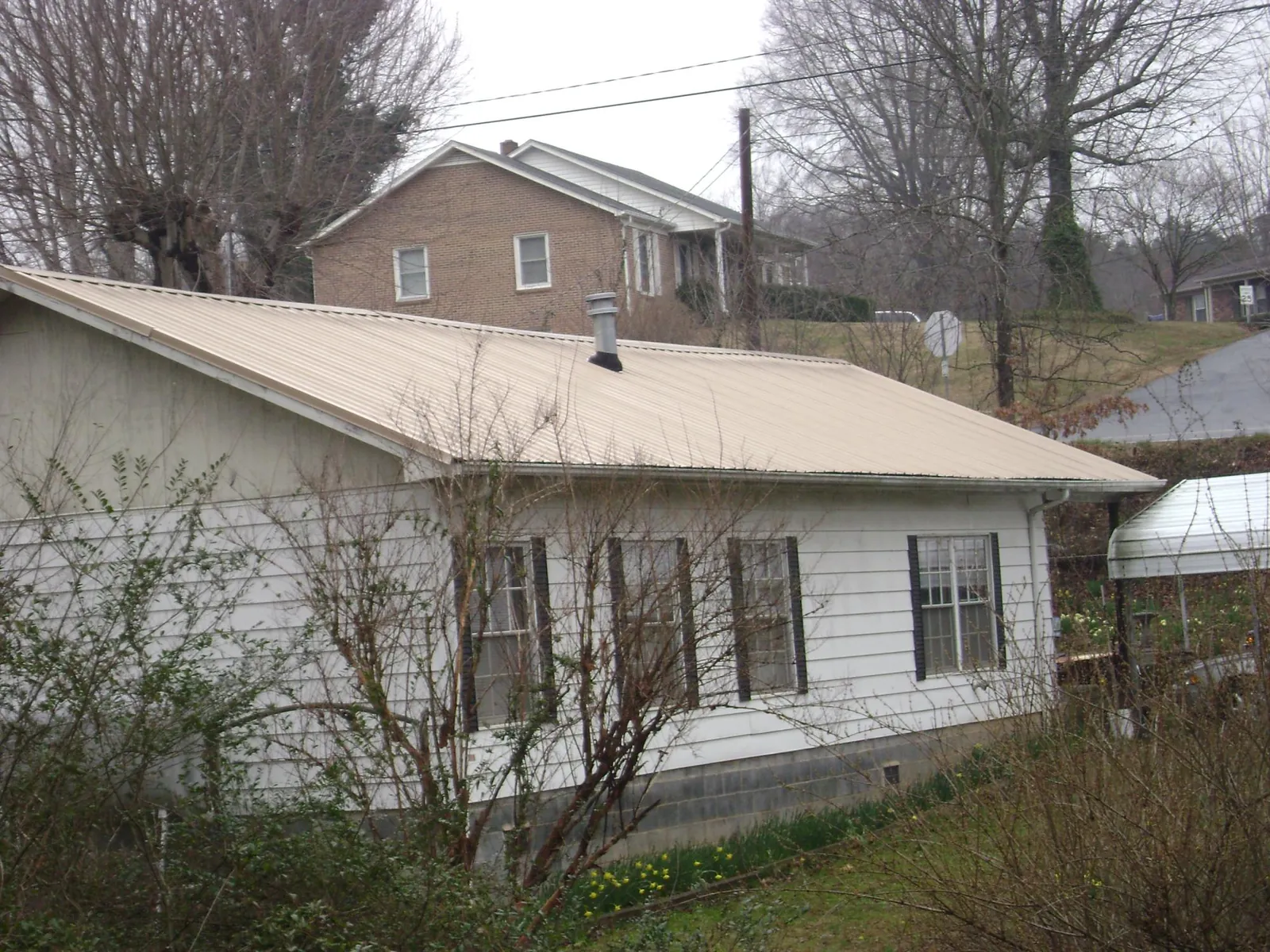 Tan metal roof on a white sided house set into a hillside — Commercial Roofing by Roofing Brothers in Bloomfield Hills